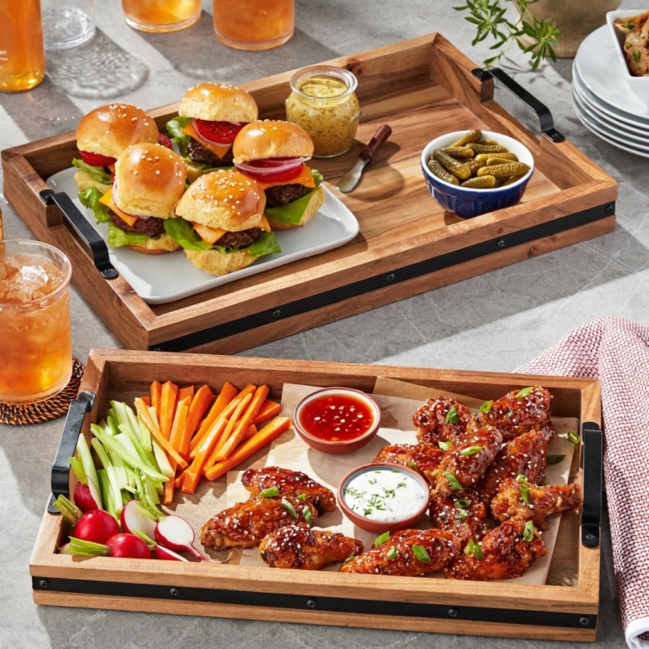 two wooden serving trays loaded with food like sliders and chicken wings